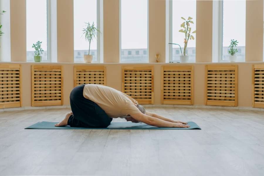 Un homme pratique la posture de l'enfant dans un studio lumineux, un moment de calme pour le yoga en voyage.
