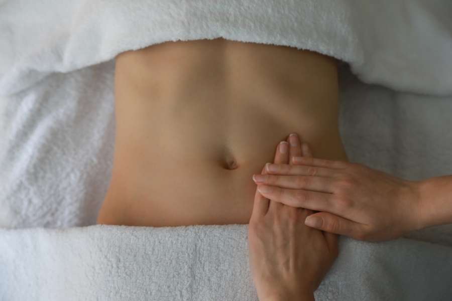 Les mains d'un massothérapeute effectuent un massage du drainage lymphatique sur le ventre d'une personne allongée sur une table de spa.