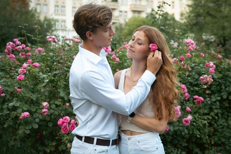 Un couple se regarde tendrement devant un rosier en fleurs.
